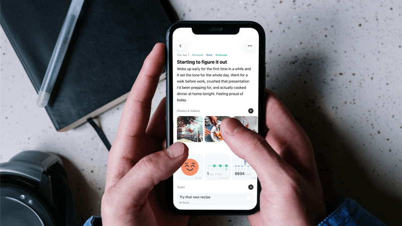 Hands holding iPhone showing Mindspace journal entry with photos and trackers