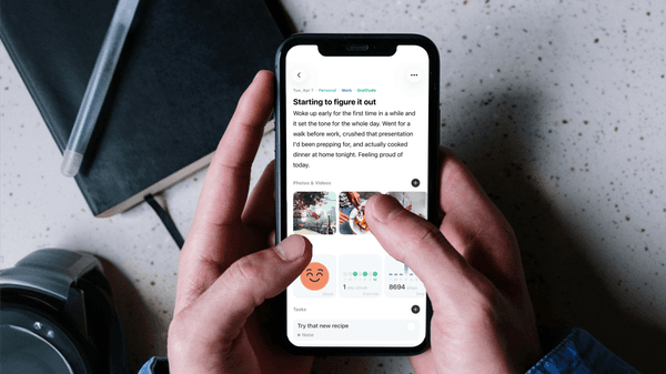 Hands holding iPhone showing Mindspace journal entry with photos and trackers